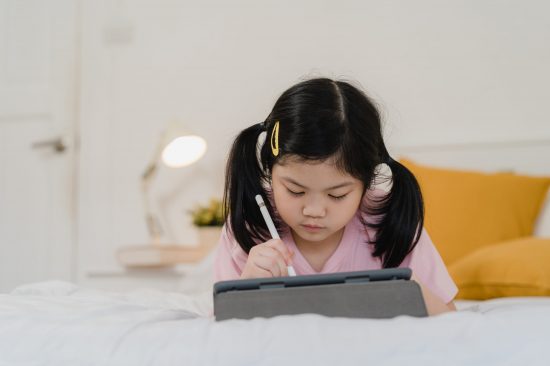 Young Asian girl drawing at home. Asia japanese woman child kid relax rest fun happy draw cartoon in sketchbook before sleep lying on bed, feel comfort and calm in bedroom at night concept.